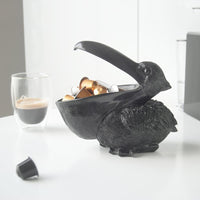 Black Peter the Pelican Home Decor by White Moose. Pictured holding coffee pods in his beak